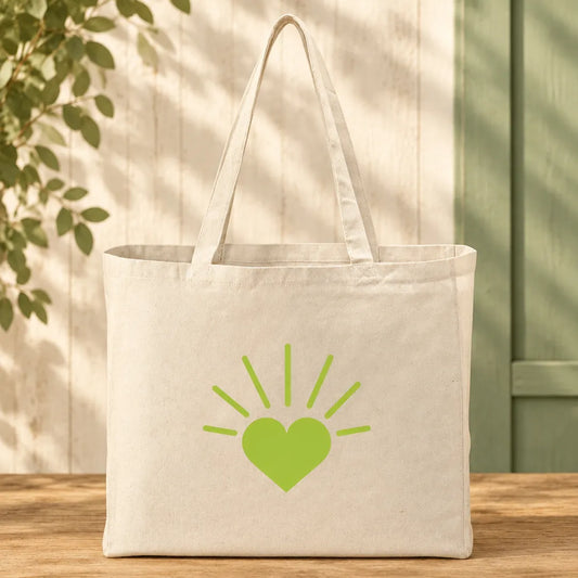 An off-white canvas tote bag with a green heart and sunburst graphic on the front, displayed on a wooden table against a light wood paneled wall with leaf shadows.