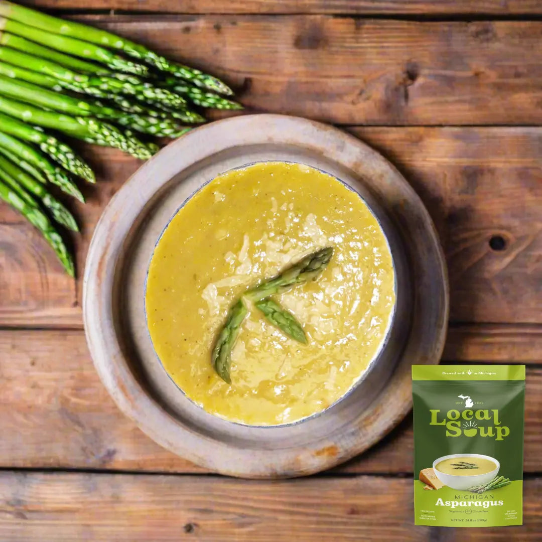 Bowl of asparagus soup with asparagus stalks on a wooden surface, featuring a 'Local Isle Soup' package.