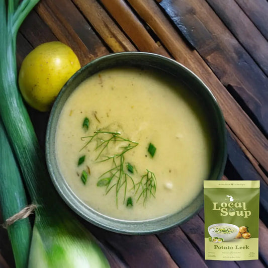 Bowl of potato leek soup with a package labeled 'Local Soup' on a wooden surface.